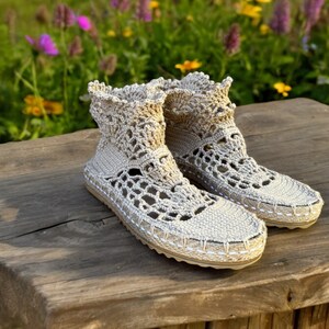 May include: A pair of beige crocheted ankle boots with a delicate lace pattern. The boots are sitting on a wooden surface.