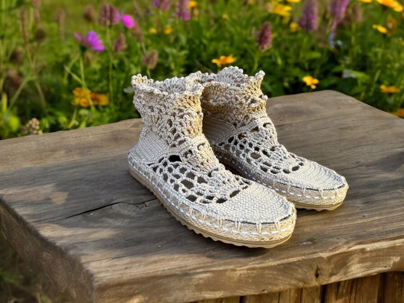 May include: A pair of beige crocheted ankle boots with a delicate lace pattern. The boots are sitting on a wooden surface.