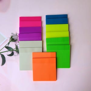 Peut inclure: Un ensemble de notes adhésives colorées dans différentes nuances de rose, violet, vert, bleu et orange. Les notes sont empilées en rangées et sont prêtes à être utilisées pour écrire des rappels, des notes ou des messages.