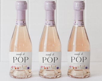 Puede incluir: Tres mini botellas de vino espumoso rosado con etiquetas que dicen "listo para POP" y presentan un diseño floral. Las etiquetas también incluyen el texto "Baby Shower de Emily".