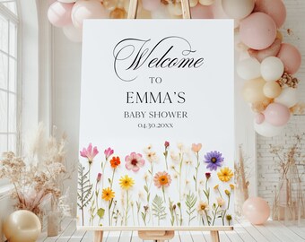 May include: Welcome to Emma's Baby Shower sign with a floral design featuring pressed flowers in shades of pink, purple, yellow, and white. The sign is displayed on an easel.