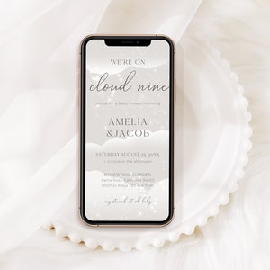 May include: A digital invitation for a baby shower with a cloud theme. The invitation reads "We're on cloud nine" and includes the names Amelia & Jacob, the date and time of the event, and the location. The invitation also includes an RSVP number and a website for the couple's registry.