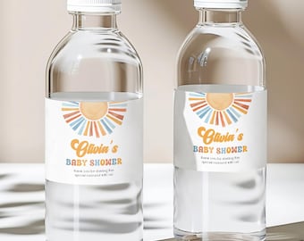 May include: Two clear water bottles with white caps. Each bottle has a label with the text "Olivia's Baby Shower" and a sunburst design in orange, blue, and yellow. The bottles are on a white surface.