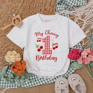 May include: White onesie with a red and white checkered number one, cherries, and the text "My Cherry 1st Birthday".
