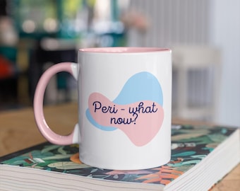 May include: White ceramic mug with a pink handle and interior, featuring the text "Peri - what now?" over a pink and blue abstract design. The mug is placed on a book with a floral cover.