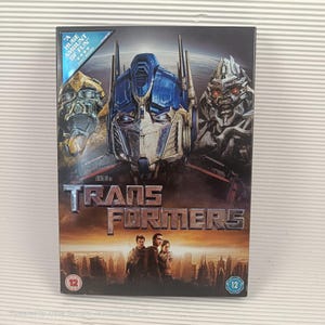 Op de afbeelding: DVD-hoesje voor de film Transformers, met afbeeldingen van de Autobots en Decepticons. De cover heeft de titel van de film en een achtergrond van een stadsgezicht. De hoes heeft een blauw en gouden sticker met de tekst "Huge Amount of Fun".