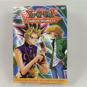 Könnte beinhalten: Eine DVD-Box der Zeichentrickserie "Yu-Gi-Oh!" mit japanischem und englischem Titel. Das Cover zeigt zwei Charaktere mit Karten, der Text lautet "3 Complete Volumes 7-9" und "9 Exciting Episodes on 3 Fantastic DVDs".