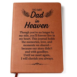 Op de afbeelding: Een bruin rechthoekig notitieboek met een leerachtige textuur en zwarte gegraveerde tekst: TO MY Dad in Heaven. Though you're no longer by my side, you'll forever live in my heart. This journal holds the memories, love, and moments we shared—because our story didn't end with goodbye. Until we meet again, I will cherish you always. Boven de tekst zijn twee vleugels gegraveerd.