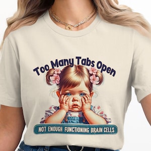 以下が含まれることがあります： ピンクの花を髪につけた少女の漫画イラストが描かれた白いTシャツ。少女の上に「Too Many Tabs Open」という文字、下に「Not Enough Functioning Brain Cells」という文字が書かれている。