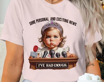 Könnte beinhalten: Hellrosa T-Shirt mit einer Grafik eines Babys mit Tiara, hinter einem Rednerpult mit Mikrofonen. Der Text "SOME PERSONAL AND EXCITING NEWS" steht über dem Baby, und "I'VE HAD ENOUGH" steht darunter.