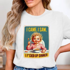 Puede incluir: Camiseta blanca con un gráfico de un bebé comiendo espaguetis y el texto "I CAME. I SAW. I F*CKED UP DINNER." El bebé está en una trona, con espaguetis en la cara y en un cuenco.
