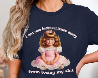 May include: A navy blue t-shirt with a pink cartoon girl and the text "I am one inconvenience away from losing my shit."