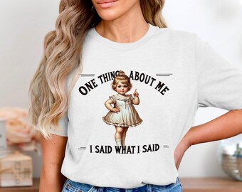 May include: White t-shirt with a graphic of a young girl with a finger pointed up and the text "One thing about me - I said what I said".