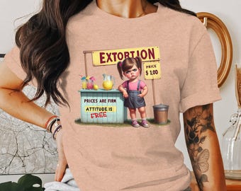 May include: A pink t-shirt with a graphic of a girl selling lemonade. The sign says "Extortion" and "Price $1.00". The sign also says "Prices are firm, Attitude is free".
