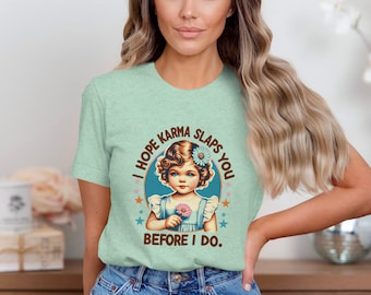 May include: A light green t-shirt with a retro-style graphic of a girl holding a flower. The graphic says "I hope karma slaps you before I do."