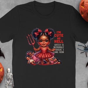 以下が含まれることがあります： 黒いTシャツ。悪魔の女の子の漫画イラストが描かれており、三叉槍を持っています。「I'M CUTE AS HELL WHICH IS INCIDENTALLY WHERE I CAME FROM」というテキストがプリントされています。ハロウィーンをテーマにしています。
