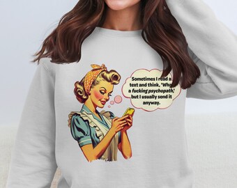 May include: A gray sweatshirt with a retro-style illustration of a woman in a blue and white dress holding a smartphone. The text on the sweatshirt reads: "Sometimes I read a text and think, 'What a fucking psychopath,' but I usually send it anyway."