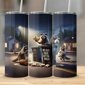 May include: A stainless steel tumbler featuring a whimsical illustration of raccoons scavenging for bread at night. The design includes the text "WE OUT HERE GETTIN BREAD" on a trash bin, with a street and houses in the background.