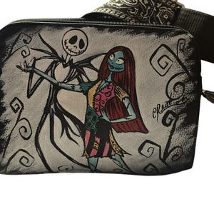 Puede incluir: Bolso bandolera negro con un dise&ntilde;o pintado a mano de Jack Skellington y Sally de Pesadilla antes de Navidad. El bolso tiene una correa negra con un dise&ntilde;o estampado y cierre de cremallera. La obra de arte est&aacute; sobre un fondo gris.