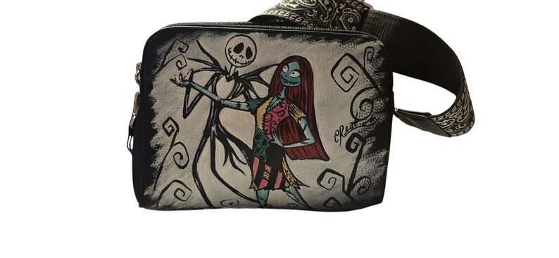 Puede incluir: Bolso bandolera negro con un dise&ntilde;o pintado a mano de Jack Skellington y Sally de Pesadilla antes de Navidad. El bolso tiene una correa negra con un dise&ntilde;o estampado y cierre de cremallera. La obra de arte est&aacute; sobre un fondo gris.