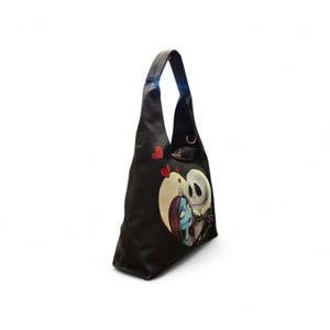 Puede incluir: Bolso de hombro negro con un gr&aacute;fico en forma de coraz&oacute;n de Jack Skellington y Sally de The Nightmare Before Christmas. El bolso tiene una sola correa y un peque&ntilde;o cierre. Tambi&eacute;n se ven acentos de coraz&oacute;n rojo.