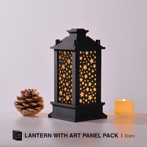Op de afbeelding: Zwarte lantaarn met een sterrenpatroon op de glazen panelen. De lantaarn is verlicht met een warme gloed. LANTERN WITH ART PANEL PACK | Stars