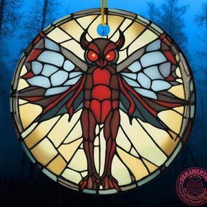 May include: A round ceramic ornament featuring a stained-glass style illustration of a red and brown moth-like creature with glowing red eyes. The design is set against a circular background of yellow and light blue geometric panels with black lines.