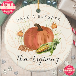 Könnte beinhalten: Runder Keramikschmuck mit Thanksgiving-Motiv. Der Schmuck zeigt eine Aquarellillustration eines Kürbisses, Mais und Mandeln mit den Worten "Have a Blessed Thanksgiving" in schwarzer Schrift. Der Hintergrund hat ein Blättermuster.