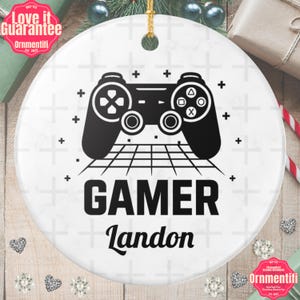 Könnte beinhalten: Runder weißer Keramik-Weihnachtsschmuck mit einem schwarzen Controller-Design, dem Wort "GAMER" und dem Namen "Landon". Enthält einen goldenen Aufhänger. Mit dem Text "Love it Guarantee" und "Ornmentifi".