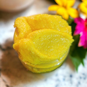 May include: A close-up of a glass jar filled with a bright yellow, smooth, and creamy substance. The substance appears to be a homemade beauty product or a food item.