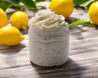 May include: A glass jar filled with a white whipped body butter, with lemons scattered around the jar on a wooden surface.