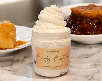 May include: A white jar of body butter with a swirl of product on top. The jar has a pink label that says "BeaCharming Body Butter Handmade - Cruelty Free - SLS Free".