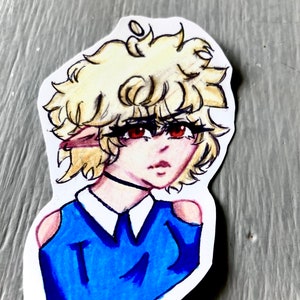 Może przedstawiać: Ręcznie rysowana naklejka przedstawiająca postać w stylu anime. Postać ma blond, kręcone włosy, czerwone oczy i nosi niebieski top z białym kołnierzem i czarnym chokerem. Naklejka znajduje się na szarej powierzchni.