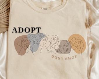 May include: A beige t-shirt with a line drawing of four dogs' faces and the text "ADOPT DON'T SHOP".