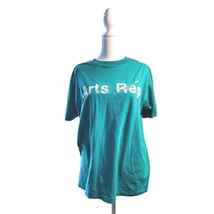 May include: Teal t-shirt with the text "Arts Prep" in white, displayed on a mannequin. The shirt has short sleeves and a crew neck. The background is plain white.