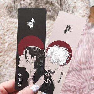 Op de afbeelding: Twee rechthoekige bladwijzers met illustraties in anime-stijl. Eén is zwart met een rode zon en een karakterprofiel, de andere is lichtroze met een rode zon en een karakterprofiel. Beide hebben Japanse tekst en een klein wit ontwerp.