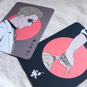May include: Two rectangular cards with anime-style illustrations. One card features a man in a white suit with a red circle background and Japanese text. The other card shows a hand and hair with a red circle background and a black background.