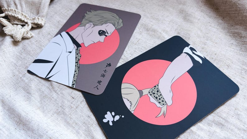 May include: Two rectangular cards with anime-style illustrations. One card features a man in a white suit with a red circle background and Japanese text. The other card shows a hand and hair with a red circle background and a black background.