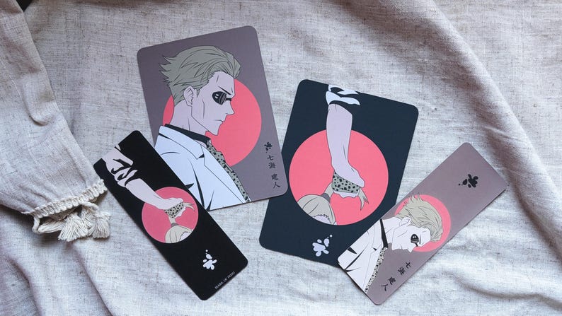 May include: Four illustrated cards and bookmarks featuring anime-style characters. The designs include a man in a white coat and a hand with a snake. The color palette includes black, pink, and gray.