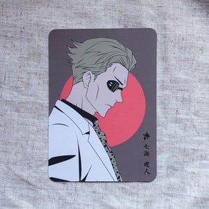 May include: A rectangular card featuring an anime-style illustration of a man in a white suit and sunglasses. The background is a dark gray with a red circle. Japanese text is visible on the right side of the card.