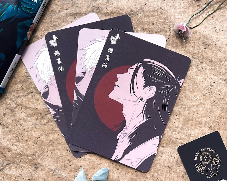 May include: Set of three playing cards featuring anime-style illustrations. Each card has a dark background with a character portrait, a red circle, and Japanese text. A small black card with white text is also present.