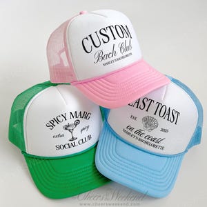 May include: Three trucker hats with white fronts and colored brims and mesh backs. One is pink with "CUSTOM Bach Club" printed on it. Another is green with "SPICY MARG extra juicy SOCIAL CLUB". The last is blue with "LAST TOAST on the coast" and a seashell graphic.