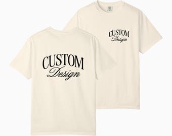 Puede incluir: Dos camisetas color crema con el texto "CUSTOM Design" impreso en escritura negra. Una camiseta muestra el texto en la parte delantera y la otra en la trasera. Las camisetas son de manga corta y tienen cuello redondo.