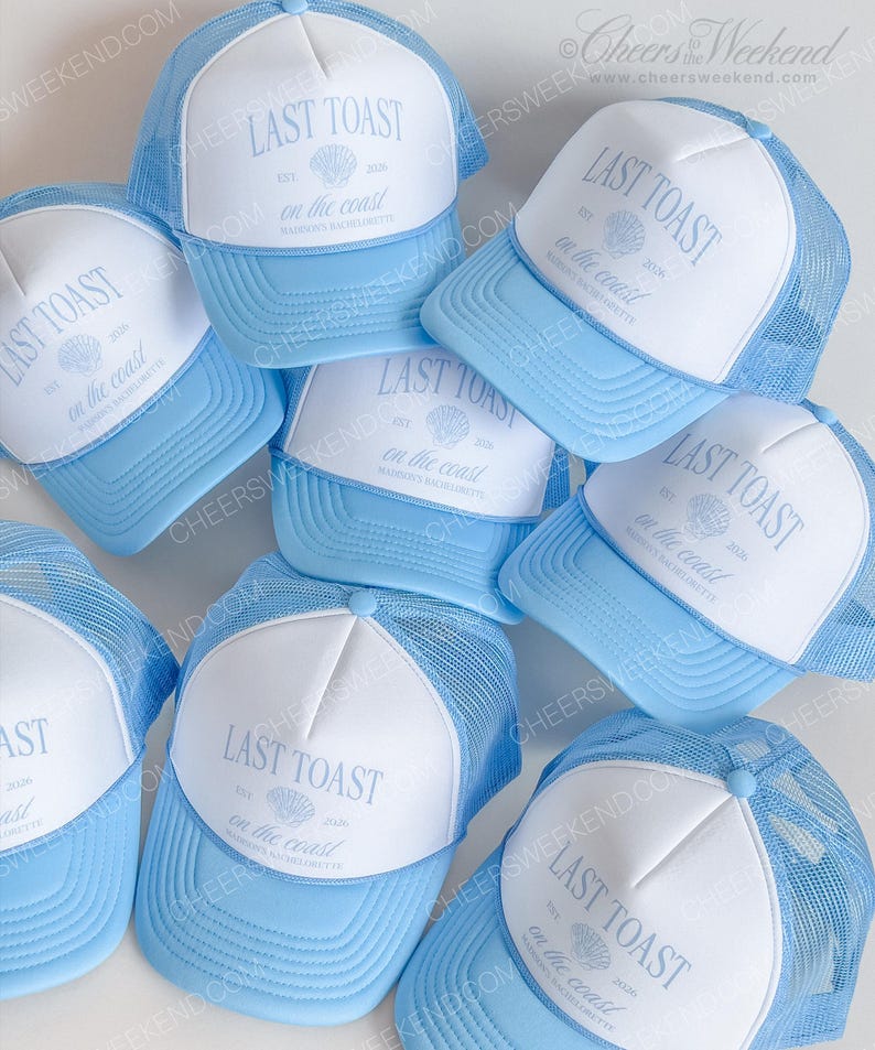 May include: A collection of light blue and white trucker hats. Each hat features a white front panel with the text "LAST TOAST" and "on the coast" printed in light blue, along with a seashell graphic. The hats have a mesh back.