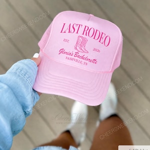 K&ouml;nnte beinhalten: Eine hellrosa Trucker-Cap mit pinkfarbenem Aufdruck, der LAST RODEO, EST. 2026, Gloria's Bachelorette und NASHVILLE, TN lautet, sowie einer Grafik von zwei Cowboystiefeln in der Mitte. Die Kappe hat ein Netzgewebe an der R&uuml;ckseite.