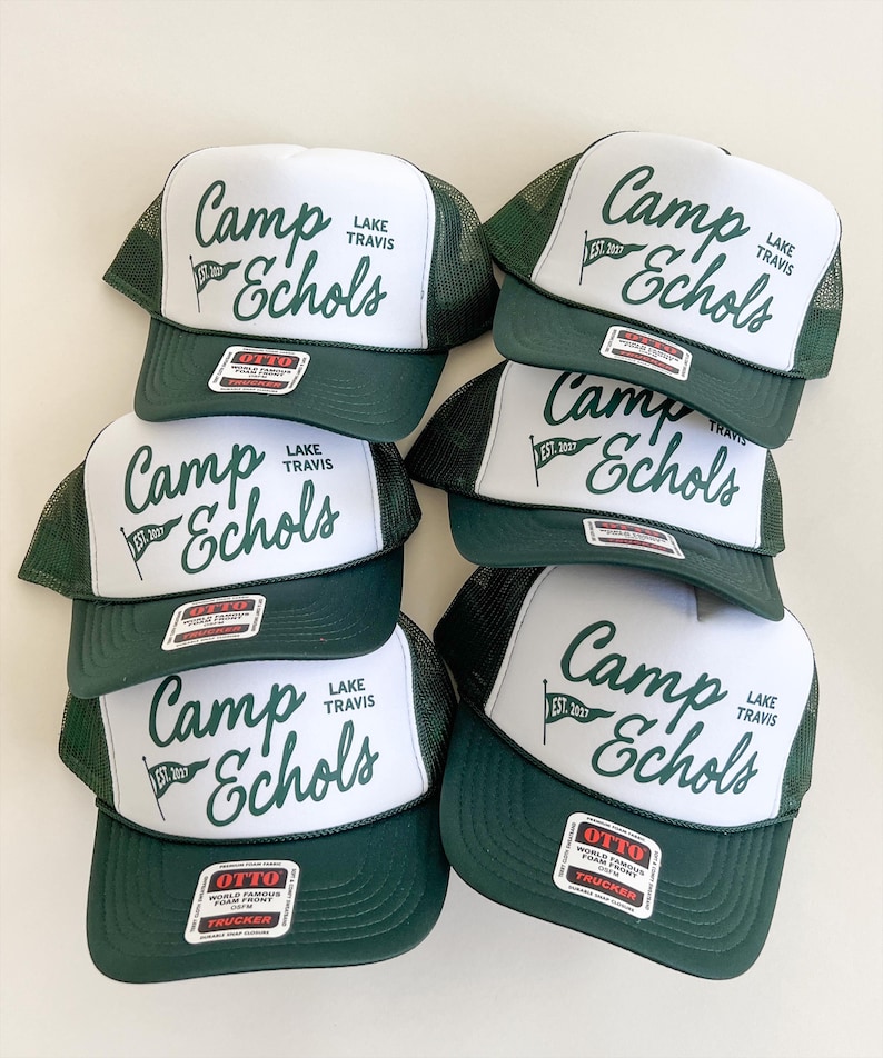 Puede incluir: Un conjunto de cinco gorras de camionero de color verde oscuro y blanco con un panel frontal de espuma blanca con el texto en verde oscuro Camp Echols Lake Travis y un icono de bandera con el texto EST. 2027. Cada gorra tiene una malla trasera.