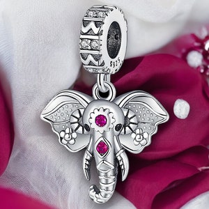May include: Silver charm featuring an elephant with pink gem accents and intricate details. The charm has a decorative silver bead at the top for attaching to a bracelet or necklace.