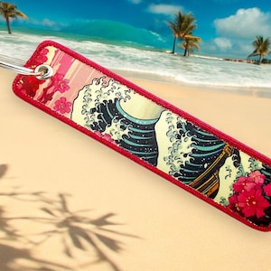 May include: Red keychain with a white background featuring a Japanese wave design with pink flowers.
