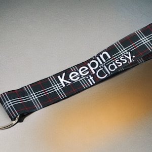 Puede incluir: Llavero de tela a cuadros en blanco y negro con una franja roja y el texto "Keepin it Classy."
