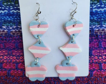 May include: A pair of dangle earrings with three layered charms. The charms are heart-shaped, diamond-shaped, and flower-shaped. The charms are painted in alternating stripes of pink, blue, and white.